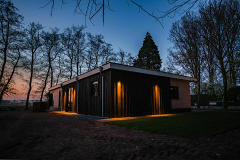 Photo du lodge Nature House à Buitengoed Ruysbos, aux Pays-Bas, illuminé et entouré d’arbres au crépuscule.