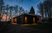 Aftenbillede af Nature House lodge ved Buitengoed Ruysbos i Holland, oplyst og omgivet af træer.