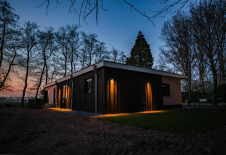 Vista nocturna del lodge Nature House en Buitengoed Ruysbos, Países Bajos, iluminado y rodeado de árboles.