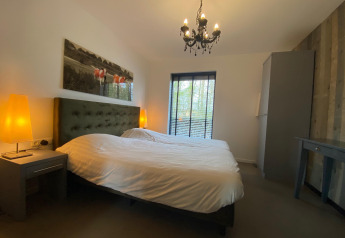 Chambre confortable avec grand lit, lumière chaude et fenêtre au Nature House, Buitengoed Ruysbos, Pays-Bas.
