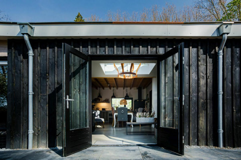 Geöffnete Doppeltür eines Nature House in Buitengoed Ruysbos, Niederlande, zeigt modernes Innendesign.