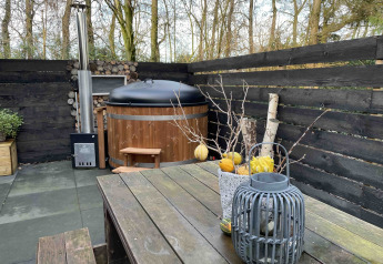 Udendørs terrasse ved Nature House, Buitengoed Ruysbos, Holland, med brændefyret badetønde og træbord.