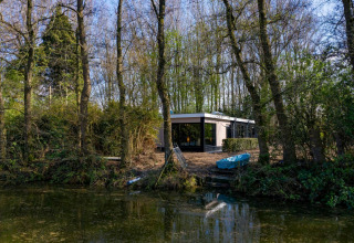 Nature House lodge at Buitengoed Ruysbos, Netherlands, surrounded by trees, next to a calm river.