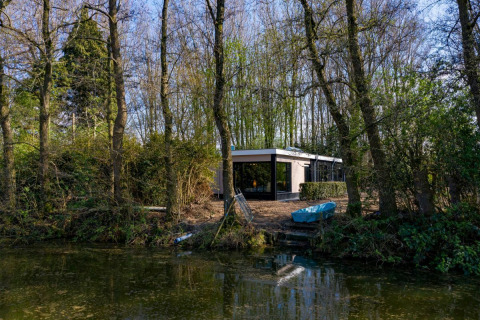 Nature House lodge at Buitengoed Ruysbos, Netherlands, surrounded by trees, next to a calm river.