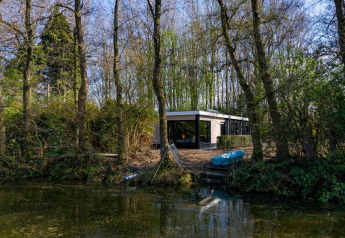 Nature House lodge at Buitengoed Ruysbos, Netherlands, surrounded by trees, next to a calm river.