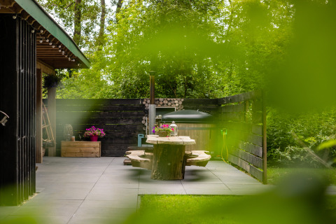 Patio exterior en Nature House de Buitengoed Ruysbos, Países Bajos, con mesa de madera y plantas verdes.