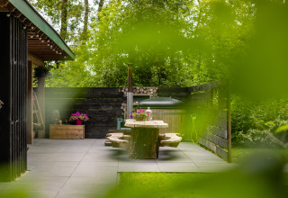 Patio exterior en Nature House de Buitengoed Ruysbos, Países Bajos, con mesa de madera y plantas verdes.