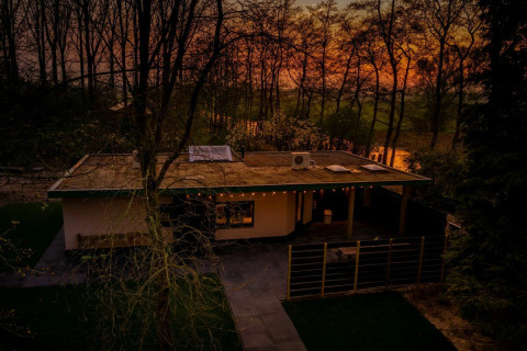 Casa lodge Nature House en Buitengoed Ruysbos, Países Bajos, al atardecer, rodeada de árboles y naturaleza.
