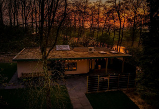 Casa lodge Nature House en Buitengoed Ruysbos, Países Bajos, al atardecer, rodeada de árboles y naturaleza.