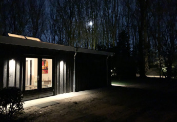 Night view of Nature House lodge at Buitengoed Ruysbos, Netherlands, with illuminated entrance and forest.