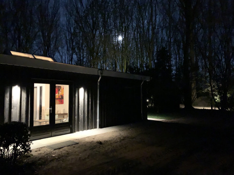 Abendaufnahme der Nature House-Lodge bei Buitengoed Ruysbos in den Niederlanden mit beleuchtetem Eingang.