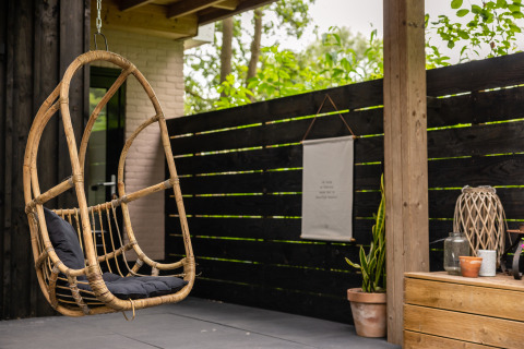 Cozy patio with hanging rattan chair and decor at Nature House lodge, Buitengoed Ruysbos, Netherlands.