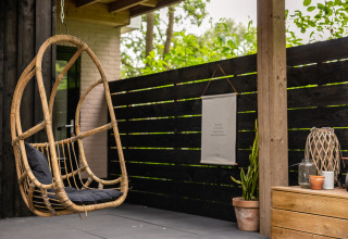 Cozy patio with hanging rattan chair and decor at Nature House lodge, Buitengoed Ruysbos, Netherlands.