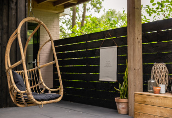Cozy patio with hanging rattan chair and decor at Nature House lodge, Buitengoed Ruysbos, Netherlands.