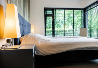 Moderne soveværelse med store vinduer, en sort seng og varme lamper på natborde i Nature House, Ruysbos.