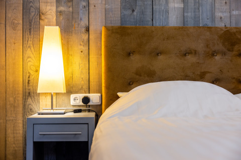 Modernes Schlafzimmer mit Holzwand, weichem Bett, Nachttisch und Lampe im Nature House in den Niederlanden.