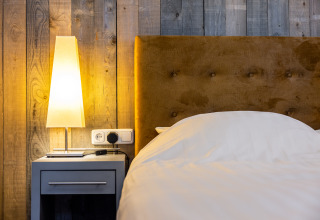 Modernes Schlafzimmer mit Holzwand, weichem Bett, Nachttisch und Lampe im Nature House in den Niederlanden.