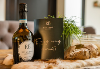 Una botella de Ruysbos Prosecco y una tarjeta con 'Enjoy every moment!' en una mesa de Nature House.