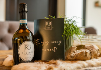 A bottle of Ruysbos Prosecco and a card reading 'Enjoy every moment!' on a table at Nature House lodge.