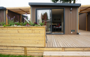 Moderne tiny house met houten veranda en bloembak bij Hotel Lodge, Holiday park De Boshoek, Nederland.