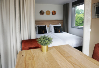 Accogliente interno tiny house all’Hotel Lodge di De Boshoek, Paesi Bassi, con letto matrimoniale e tavolo.