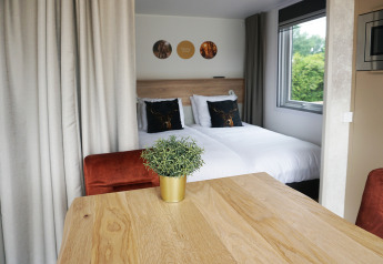 Gezellig tiny house interieur bij Hotel Lodge, Holiday park De Boshoek, Nederland met bed en houten tafel.