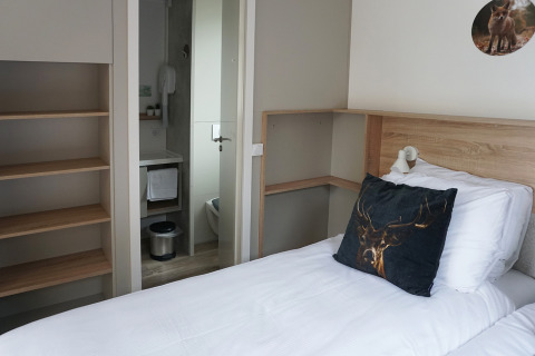 Compact hotel room at Hotel Lodge in De Boshoek, Netherlands, showing single bed, shelves, and bathroom.