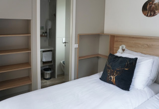 Compact hotel room at Hotel Lodge in De Boshoek, Netherlands, showing single bed, shelves, and bathroom.
