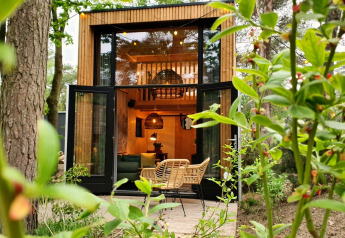 Tiny House bij Maasduinen in Nederland met openstaande deuren, moderne stoelen en veel groen buiten.