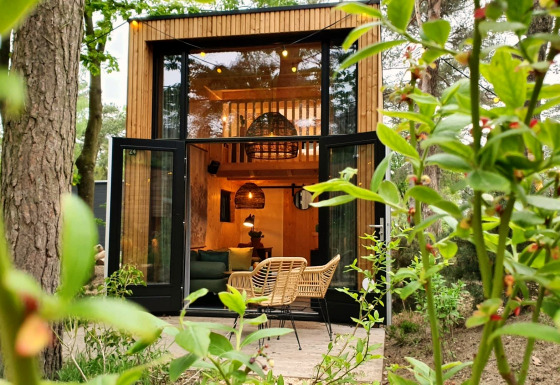 Tiny House bij Maasduinen in Nederland met openstaande deuren, moderne stoelen en veel groen buiten.