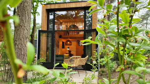 Tiny House en Maasduinen, Países Bajos, con puertas abiertas, sillas modernas y vegetación exuberante.