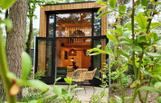 Tiny House ved Maasduinen i Holland med åbne døre, træstole foran og frodige planter omkring.