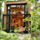 Tiny House bij Maasduinen in Nederland met openstaande deuren, moderne stoelen en veel groen buiten.