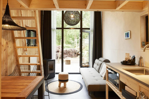 Moderna tiny house en Maasduinen, Holanda, con interior de madera, cocina, sofá y ventanales grandes.