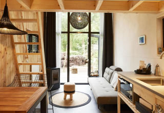 Moderne tiny house in Maasduinen, Nederland, met houten interieur, keuken, zetel en grote ramen.