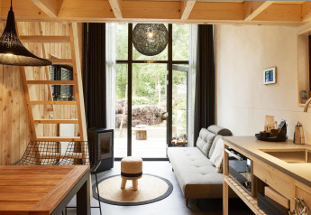 Moderne tiny house i Maasduinen, Holland, med trægulve, loft, sofa, spiseområde og store vinduer.