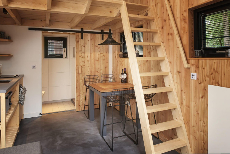 Interior de Tiny House at Maasduinen en los Países Bajos con paredes de madera, escalera y comedor.