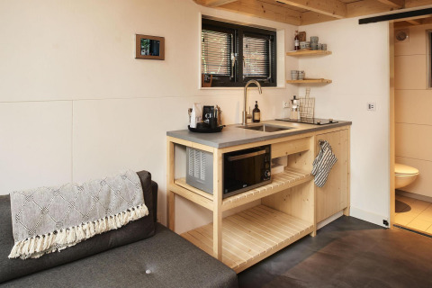 Moderne minikøkken og stue med sofa i Tiny House ved Maasduinen, Holland, med træ og enkle detaljer.