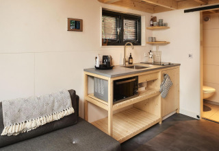 Moderne keuken en zitruimte in een tiny house aan Maasduinen, Nederland, met lichte houten afwerking.