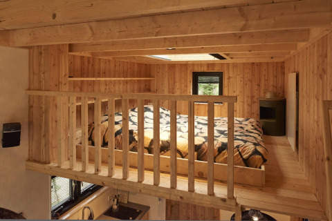 Altillo para dormir en la Tiny House de Maasduinen, Países Bajos, con paredes de madera y tragaluz