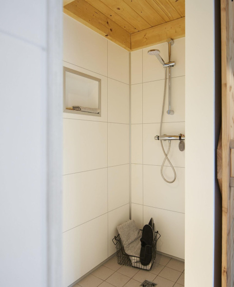 Moderne douche in Tiny House bij Maasduinen, Nederland, met houten plafond en witte tegels.