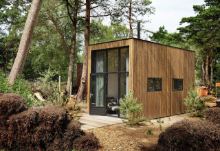 Casa pequeña moderna con fachada de madera en un entorno boscoso en Maasduinen, Países Bajos, de día.