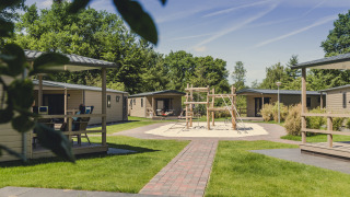 Buitenaanzicht van 6x bungalette lodge op Vakantiepark Mölke in Nederland, met speeltuin en groene omgeving.