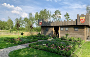Houten lodge in kasteelstijl bij vakantiepark 't Rheezerwold, omringd door kleurrijke tuinen.
