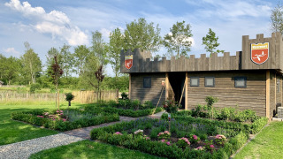Houten lodge in kasteelstijl bij vakantiepark 't Rheezerwold, omringd door kleurrijke tuinen.