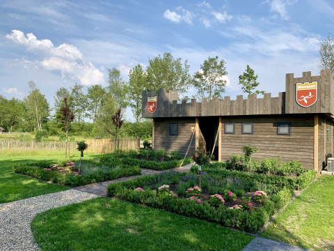 Houten lodge in kasteelstijl bij vakantiepark 't Rheezerwold, omringd door kleurrijke tuinen.