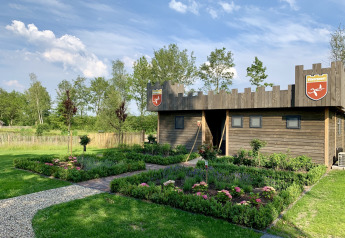 Houten lodge in kasteelstijl bij vakantiepark 't Rheezerwold, omringd door kleurrijke tuinen.