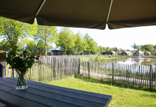 Vista desde una terraza con flores en la mesa hacia el estanque y lodges en Holiday Park 't Rheezerwold.
