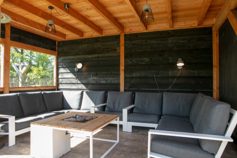 Overdekte loungehoek met grijze zetel, houten plafond en tafel bij Castle the Pond Gate, Nederland.