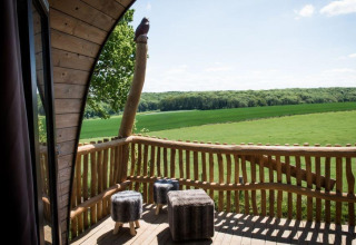 Vue depuis la tiny house Treelodge au Gulperberg, Pays-Bas, avec terrasse en bois et champs verdoyants.
